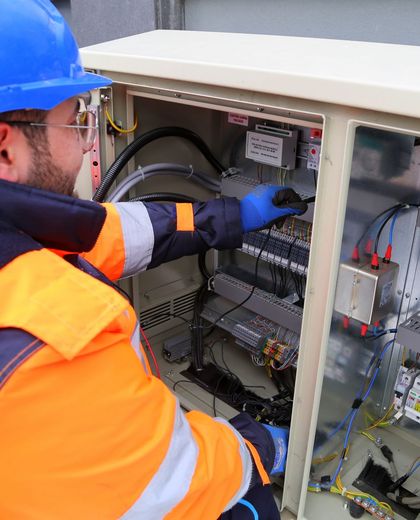 Eletricista de capacete e luvas trabalhando no quadro elétrico